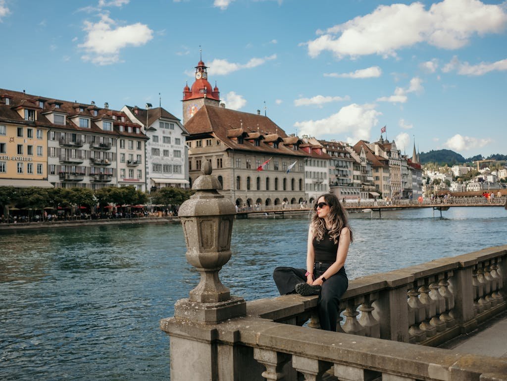 A woman sitting on a railing overlooking a river and buildings